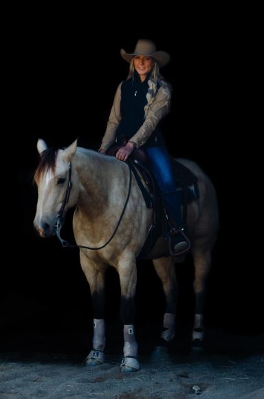 A person in a cowboy hat riding a light-colored horse in low light.